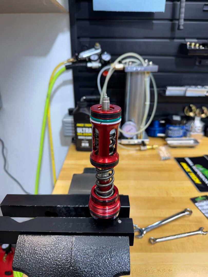 Close-up of a red mechanical component held in a vise on a workbench.