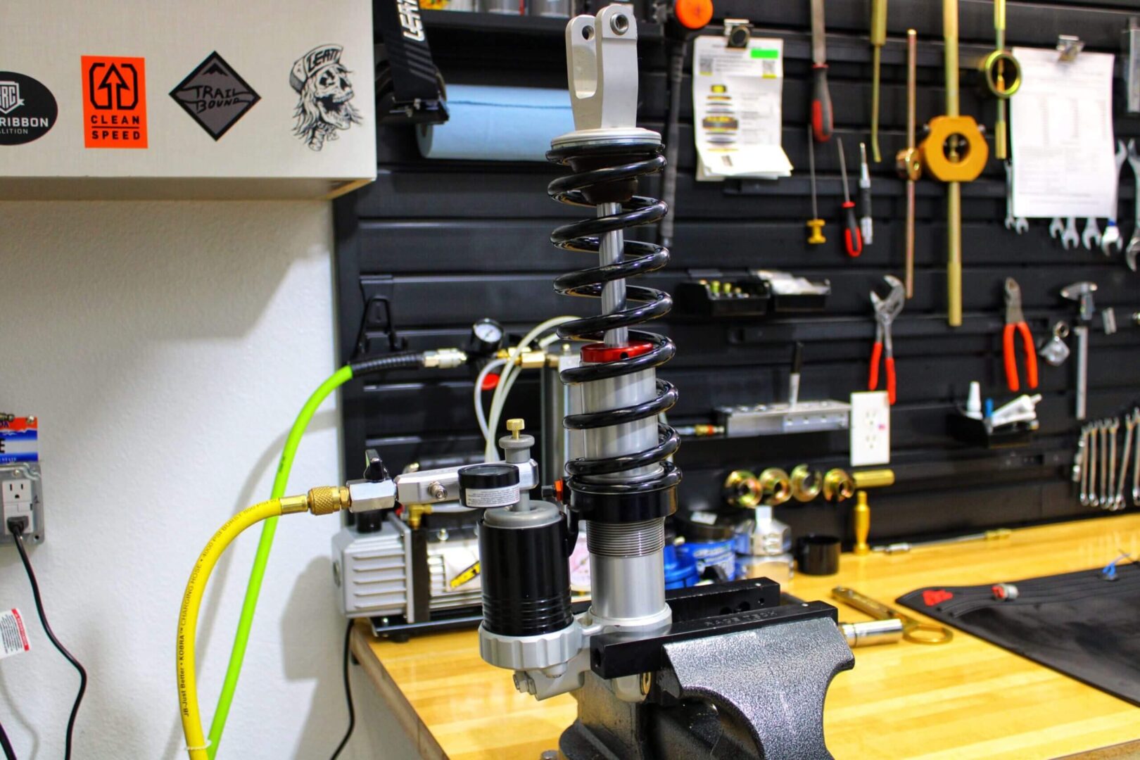 Close-up of a mechanical shock absorber on a workbench with tools in the background.